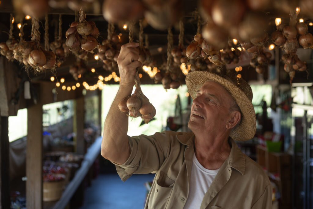 Older man looking at onions hanging from the ceiling of a food stand