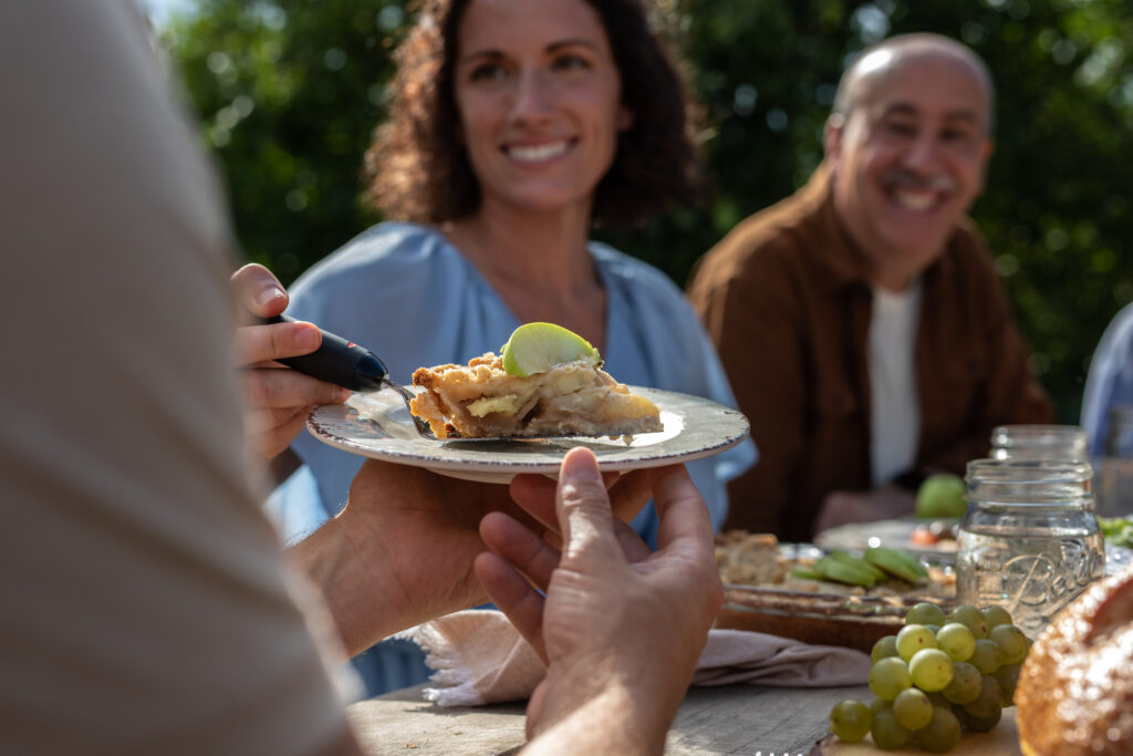 Family having meal outside. Woman putting a piece of apple pie on plate