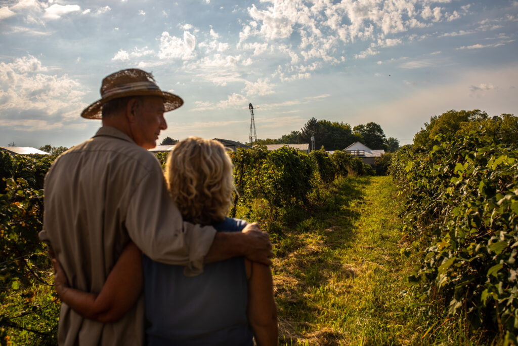 Mature couple looking out over farm field. House in the distance.