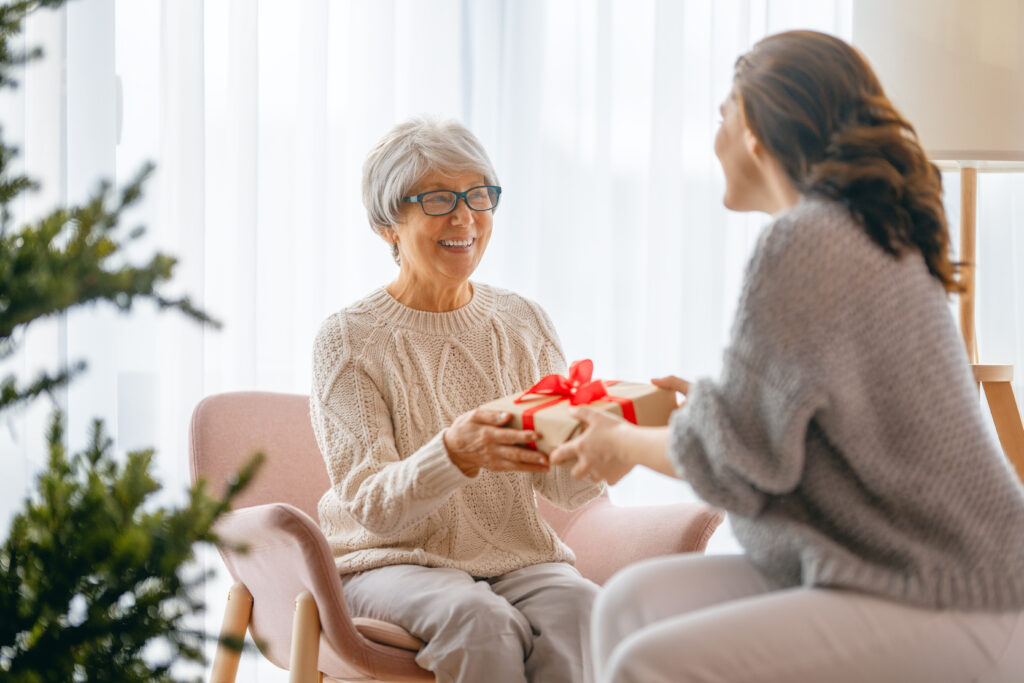 Older woman receiving a wrapped gift from another person in a cozy living room.