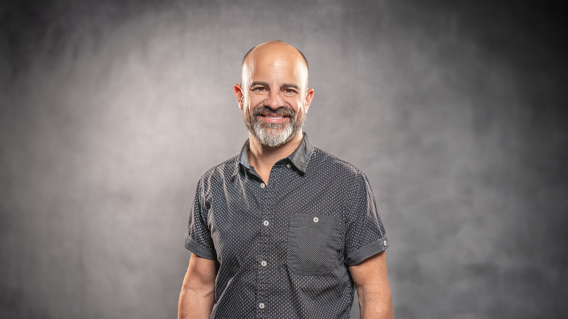 Smiling man standing against a gray studio background.